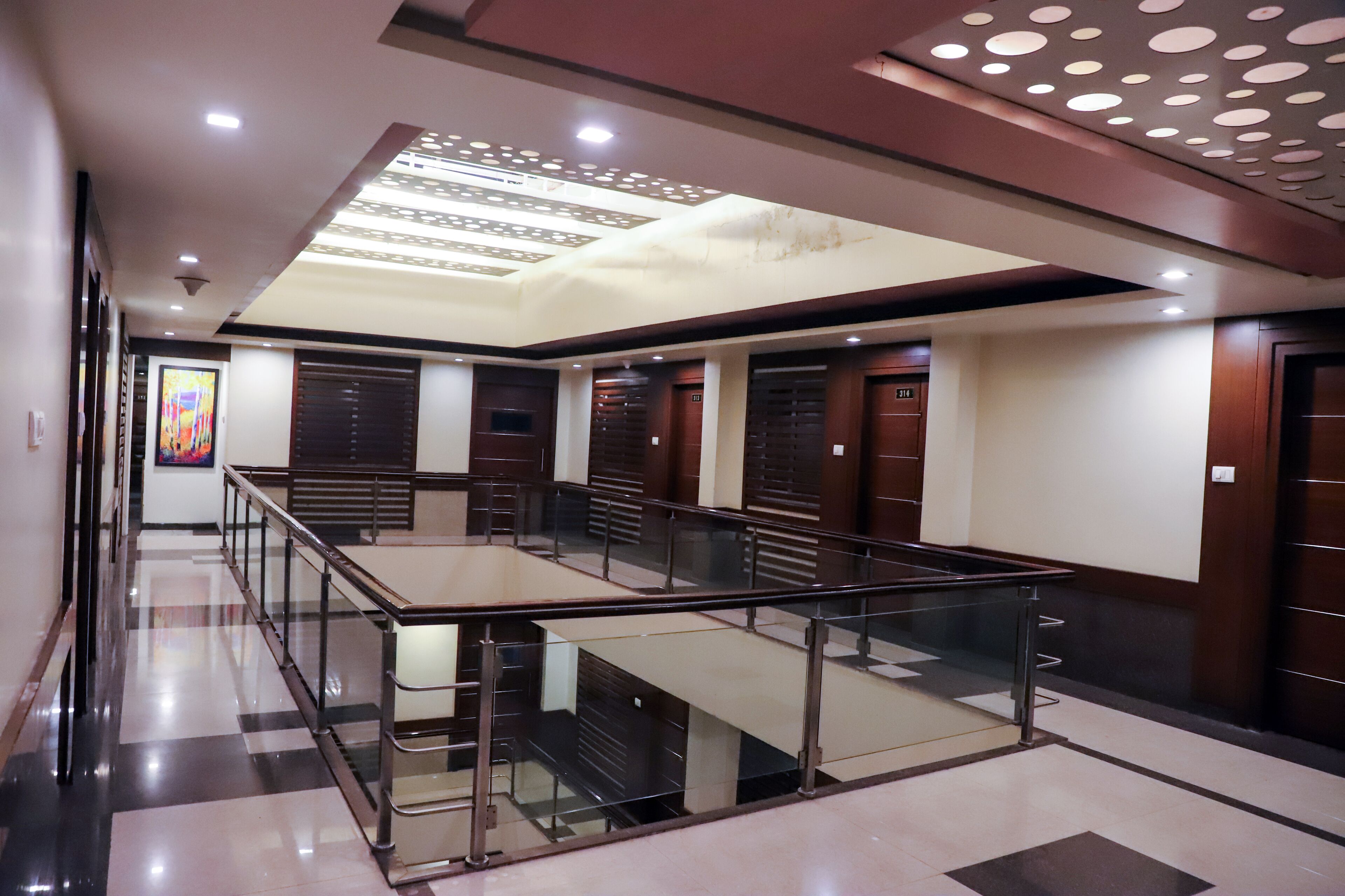 A hotel lobby with a glass railing, check-in counters, and a ceiling with circular cutouts.