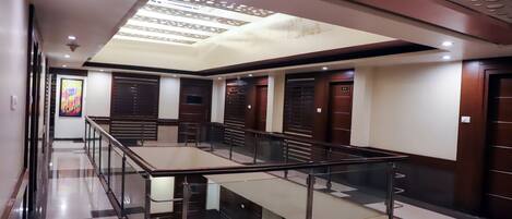 A hotel lobby with a glass railing, check-in counters, and a ceiling with circular cutouts.