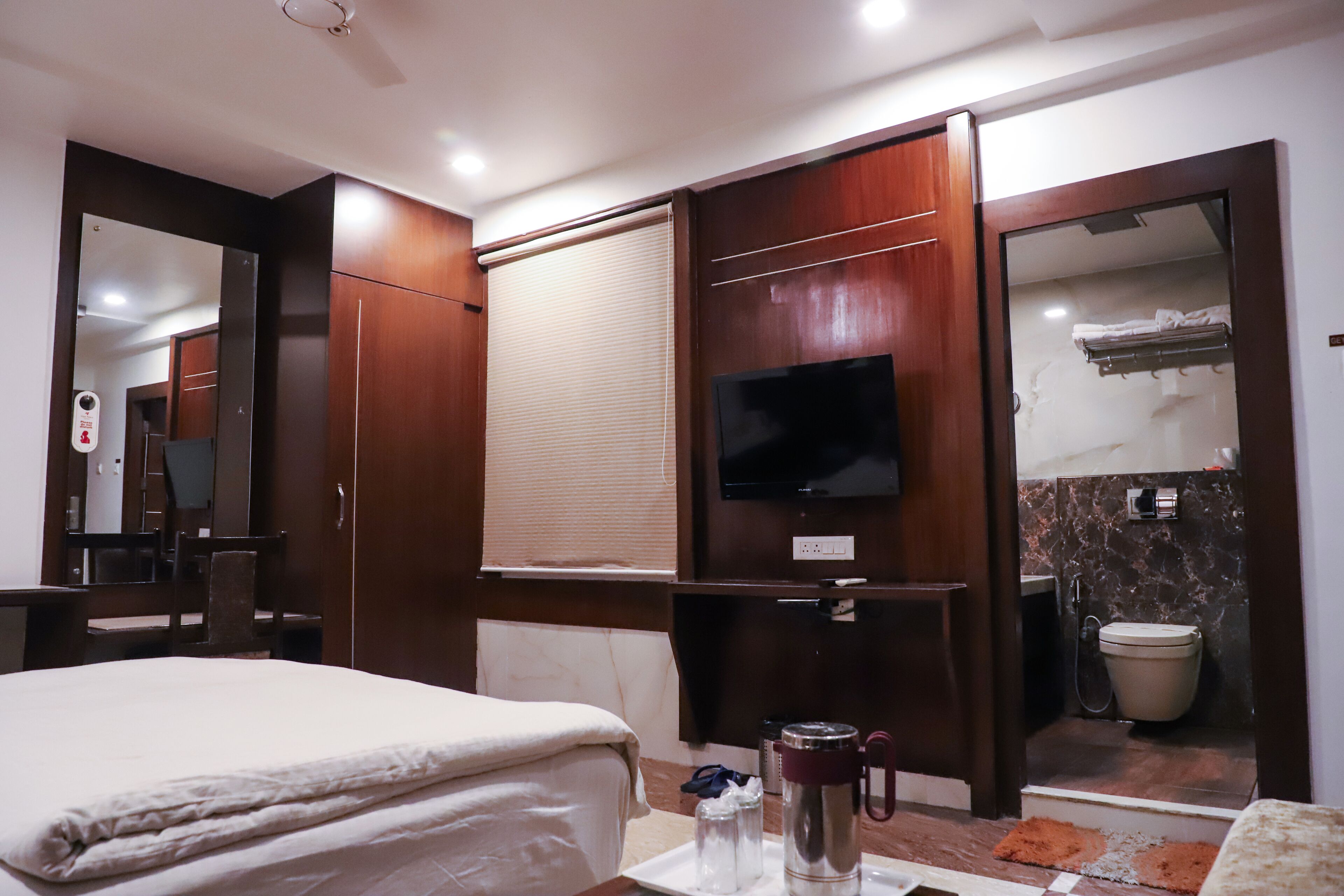 Ein Hotelzimmer mit Bett, Wandfernseher, Badezimmer mit Toilette und Waschbecken sowie einem Spiegel.