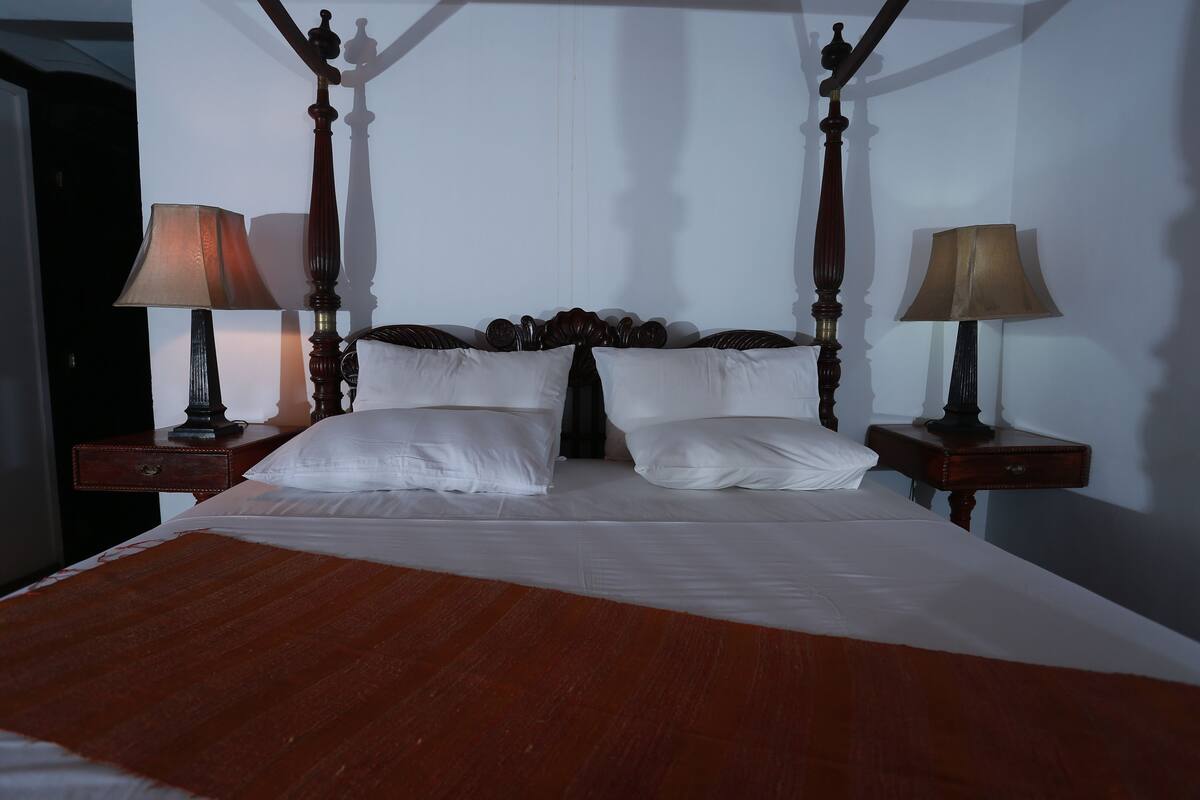 A four-poster bed with white linens and two bedside tables with lamps.