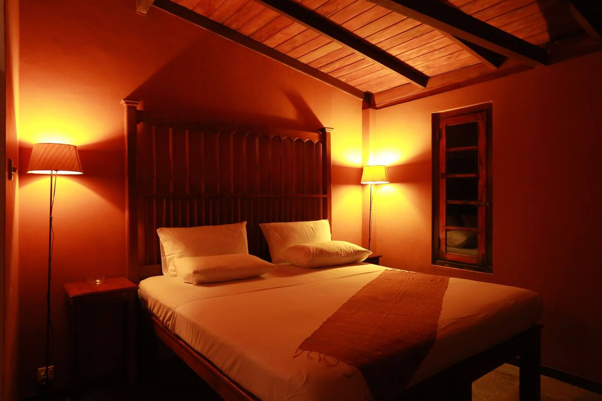 A bedroom with a wooden headboard, two bedside lamps, and a window with a wooden frame.