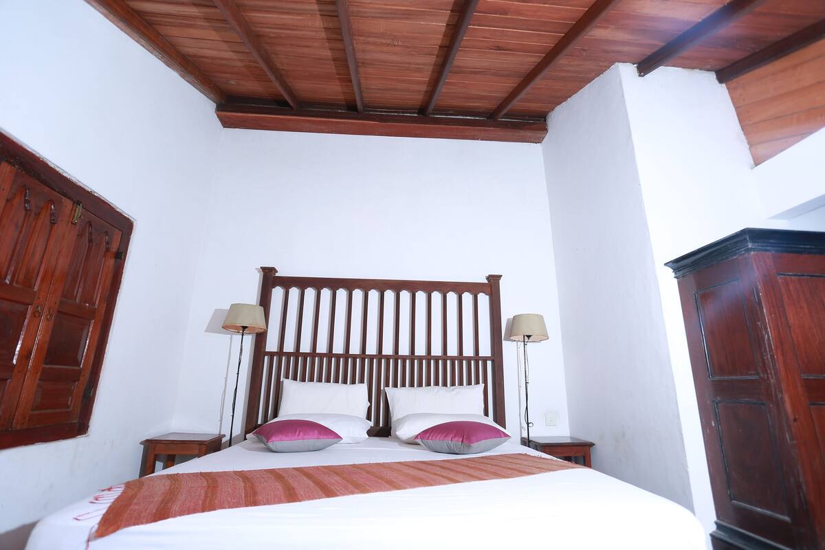 A bedroom with a wooden headboard, two bedside tables with lamps, and a bed with white bedding and pink pillows.