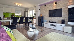 A modern living room with a glass coffee table, a sofa, a flat-screen TV mounted on a stone wall, and a dining area with chairs and a table. - Villa Margherita (Kanfanar)