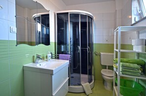 Een badkamer met een hoekdouche, toilet, wastafel en een groen opbergrek.