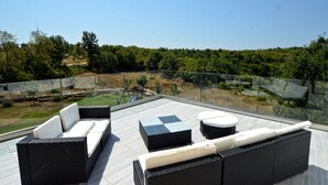 A rooftop terrace with wicker furniture, a glass barrier, and a view of a landscaped area. - Villa Margherita (Kanfanar)
