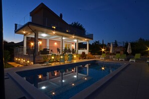 Een modern huis met een zwembad, buiten zitplaatsen en een overdekt terras.