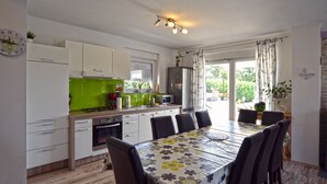 A modern kitchen with white cabinets, a green countertop, and a dining area with a floral tablecloth and six chairs. - Villa Margherita (Kanfanar)