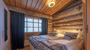 Un dormitorio de cabaña de troncos con dos camas, una ventana con cortinas y un techo de madera.