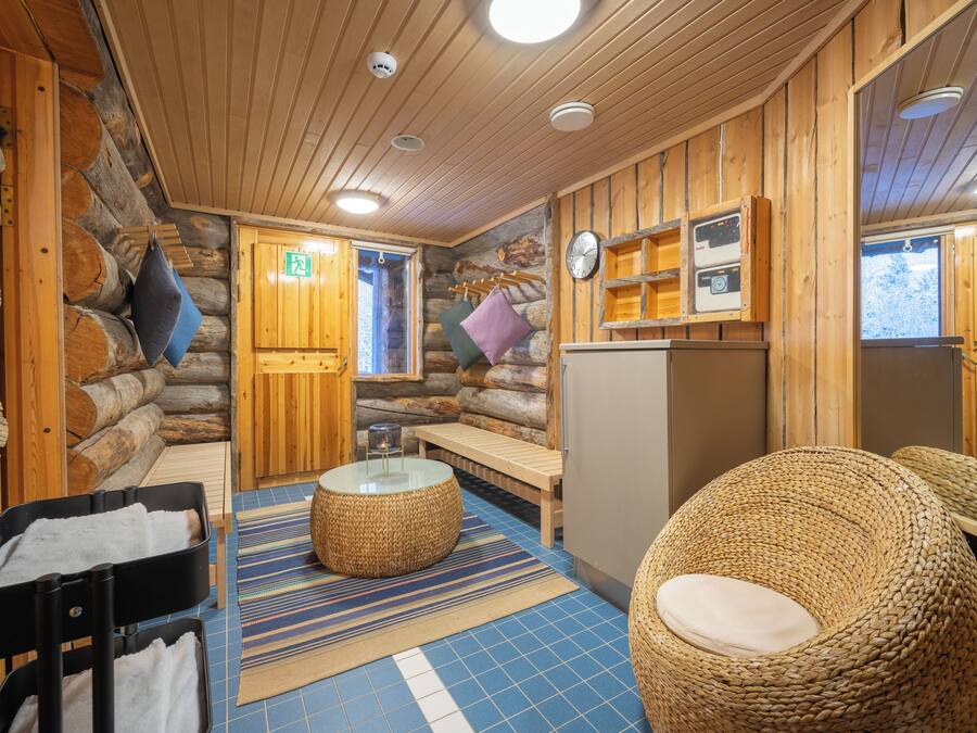 L’intérieur d’une cabane en rondins, avec un mur en pierre, un plafond en bois, un banc rond en osier, une petite table ronde et un banc agrémenté de coussins.