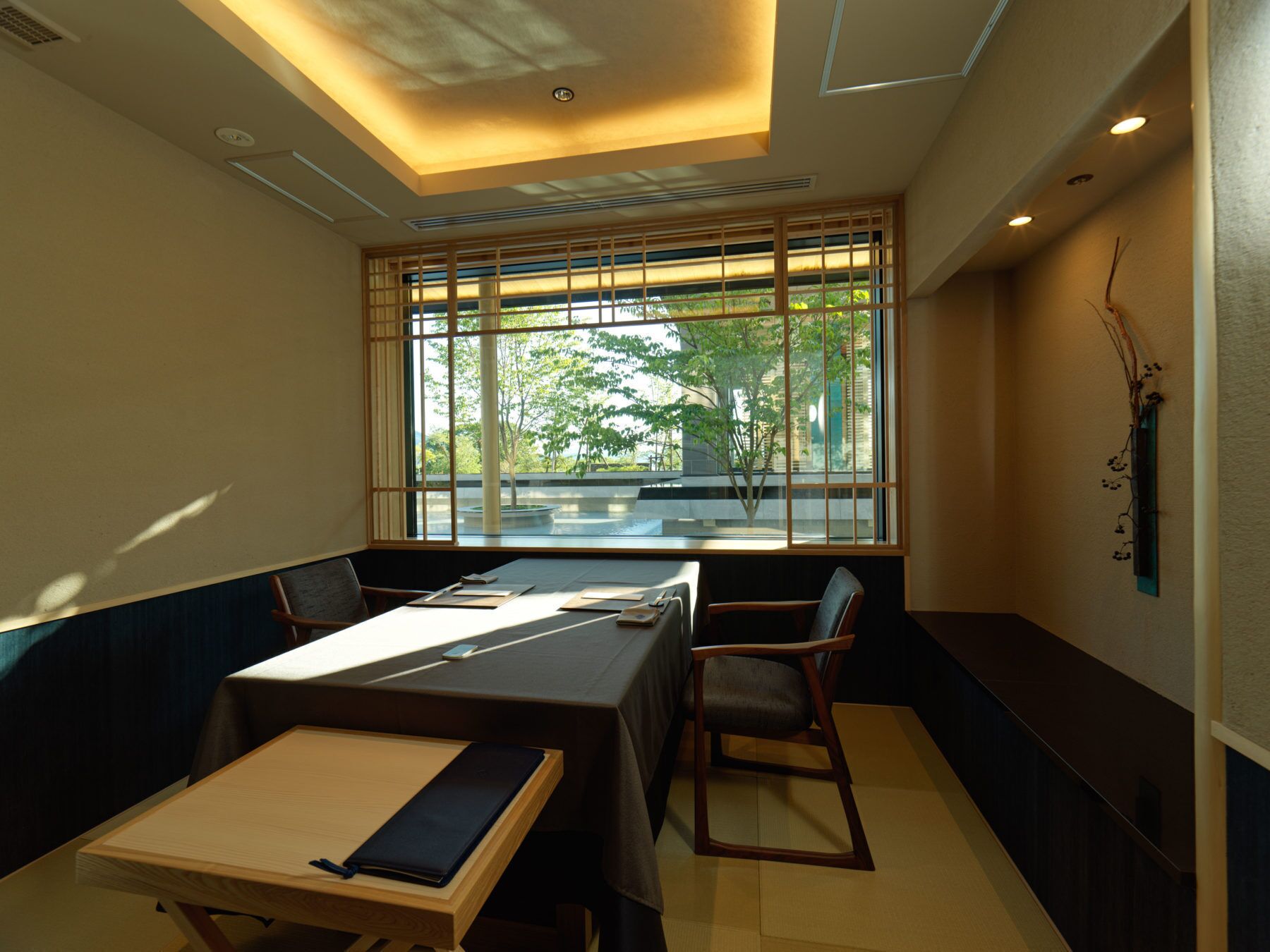 A dining area with a table and chairs, a view of greenery outside, and a ceiling with recessed lighting.