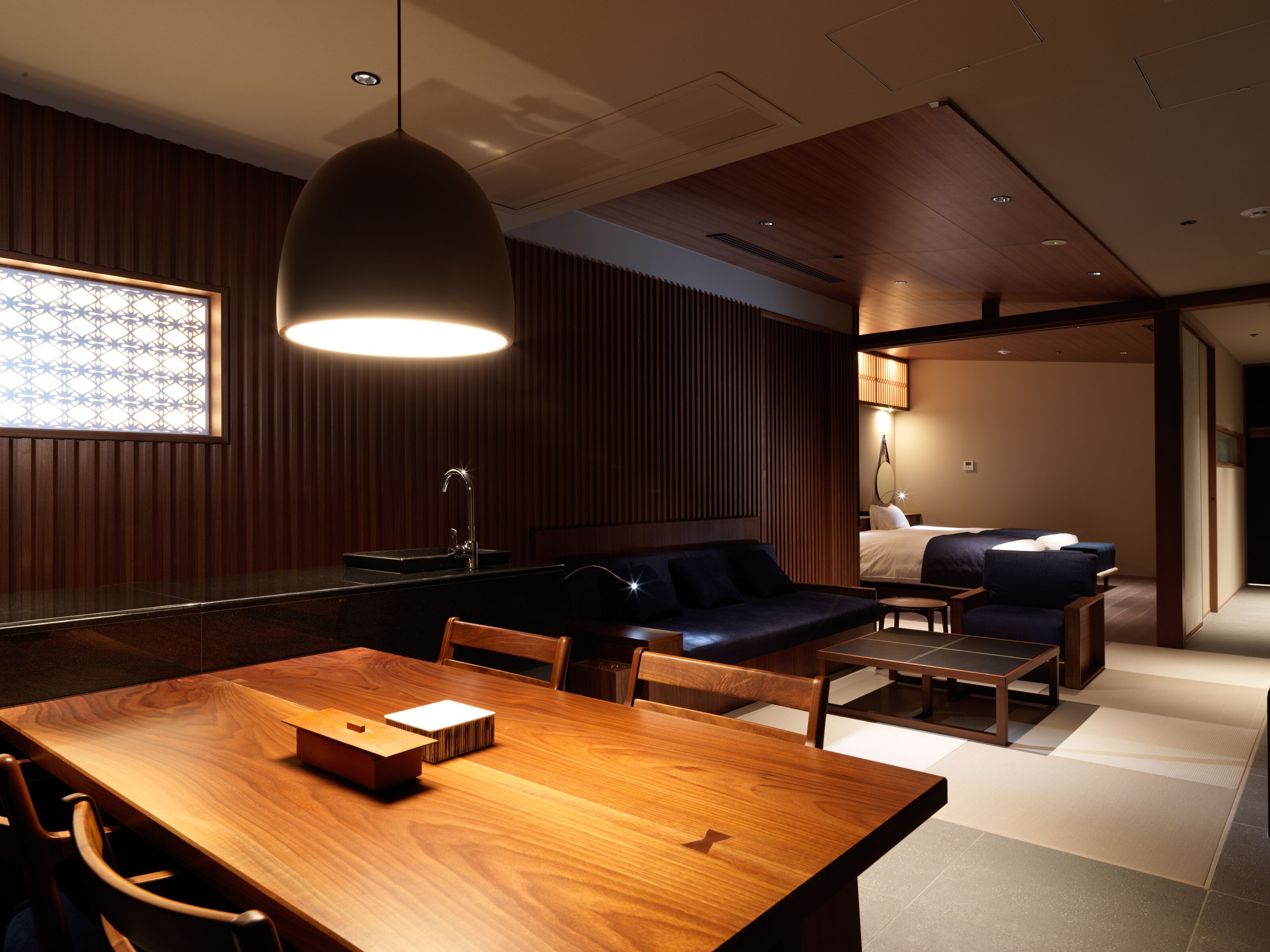 Una habitación de hotel moderna con una mesa de comedor de madera, un sofá y una pequeña zona de estar.