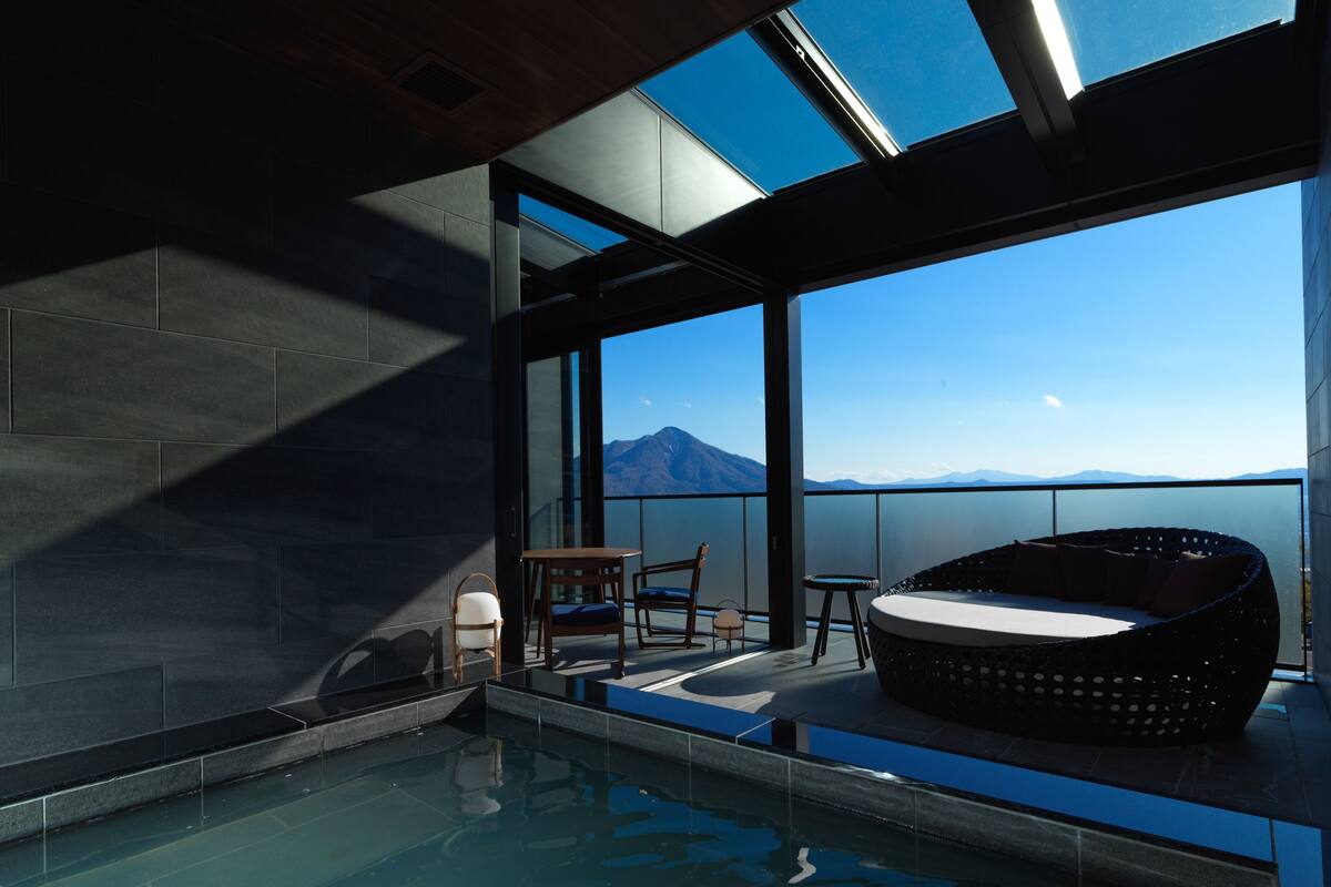 A modern indoor pool area with a view of mountains, a seating area, and a glass-enclosed space.