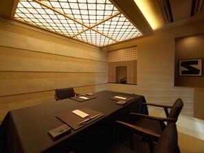 Une salle de conférence avec une longue table, des chaises, une grande fenêtre à carreaux et un cadre contenant une lettre accroché au mur.