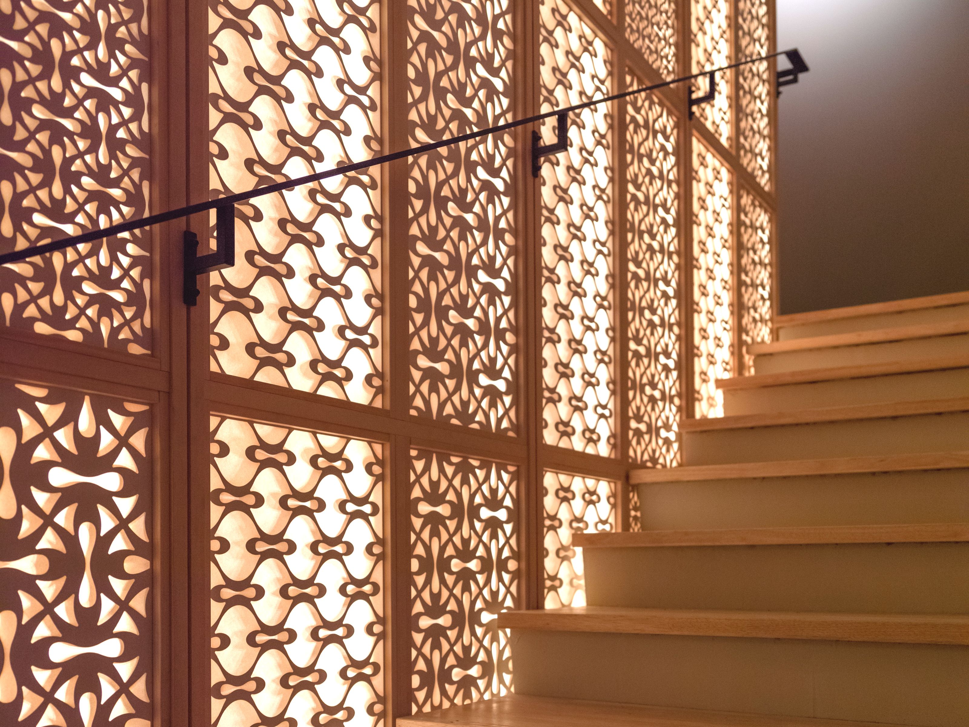 Un escalier avec des marches en bois et un panneau décoratif en bois orné de motifs complexes découpés.