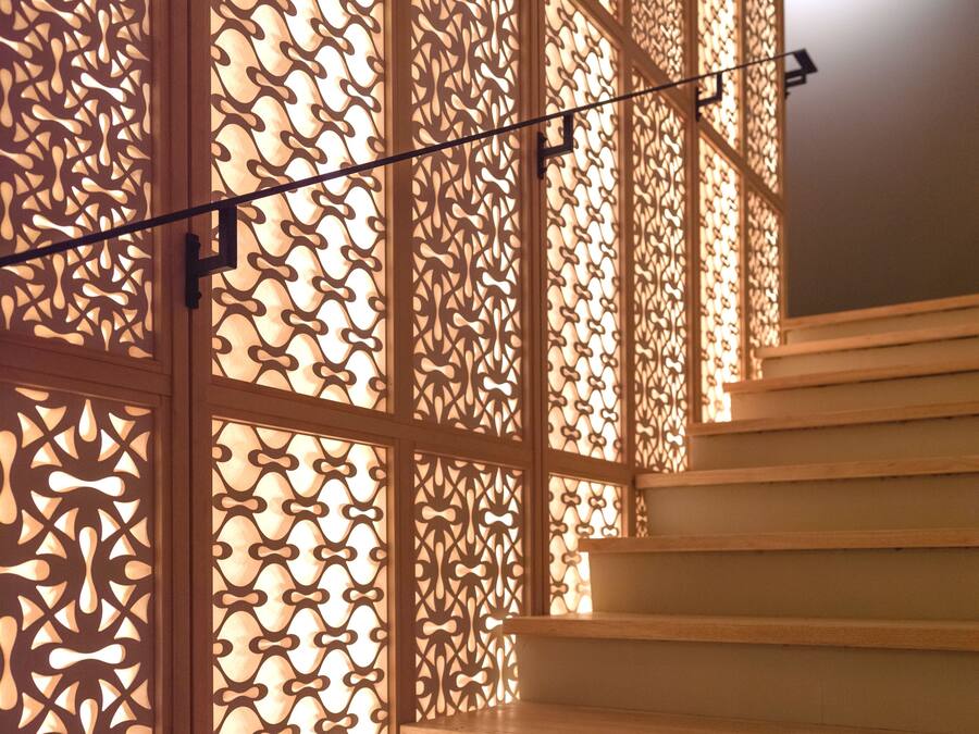 Un escalier avec des marches en bois et un panneau décoratif en bois orné de motifs complexes découpés.