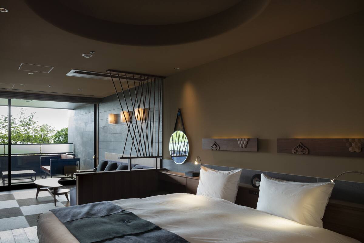 A modern hotel room with a large bed, a seating area with a view, and a balcony.