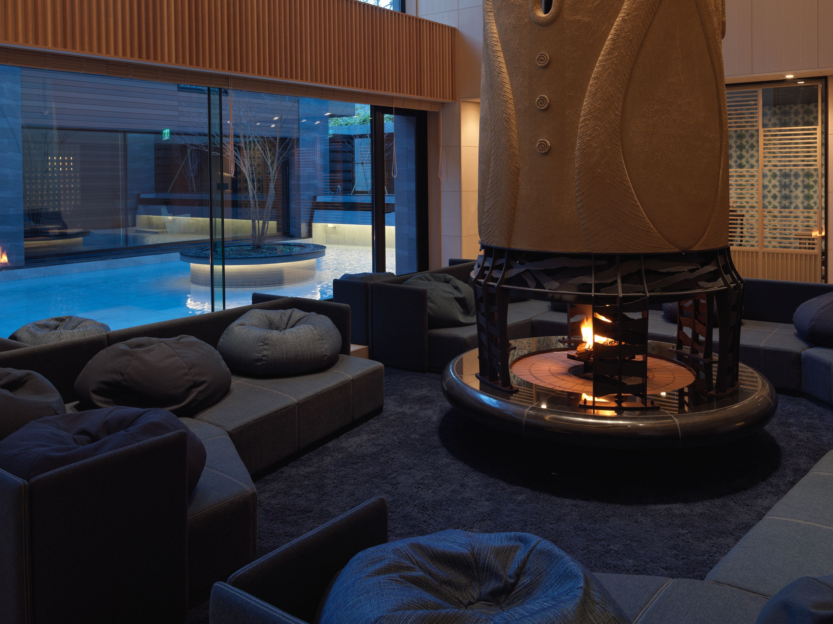 A modern lounge area with a glass-enclosed pool, comfortable seating, and a central fire feature.
