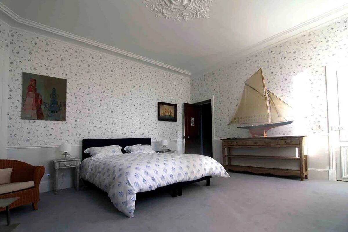 A bedroom with a bed, a nightstand, a dresser, a chair, and a sailboat model.