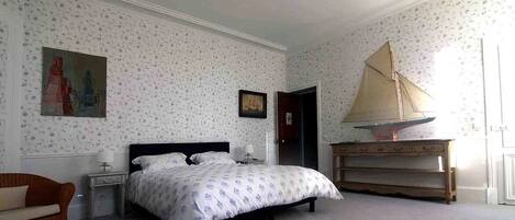 Une chambre à coucher comprenant un lit, une table de chevet, une commode, une chaise et une maquette de voilier.