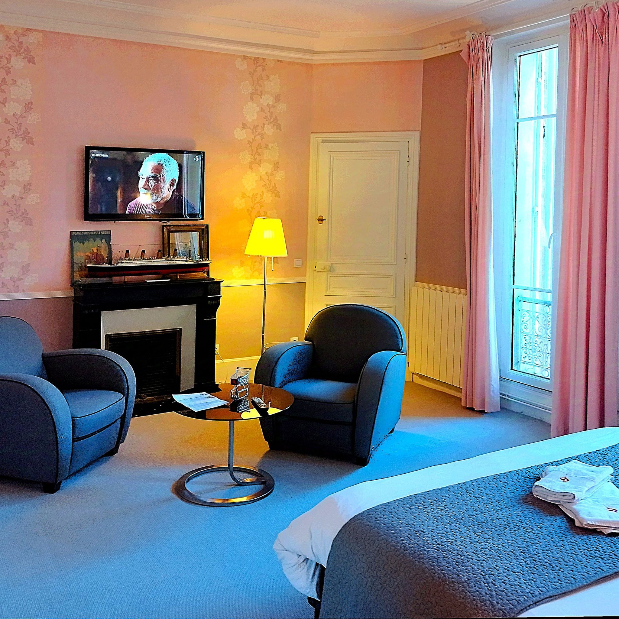 Ein Hotelzimmer mit Fernseher, Kamin, zwei Sesseln, einem kleinen Tisch und einem Bett.