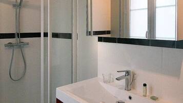 Un baño moderno con ducha de vidrio, un lavamanos blanco con espejo y un perchero con toallas dobladas.