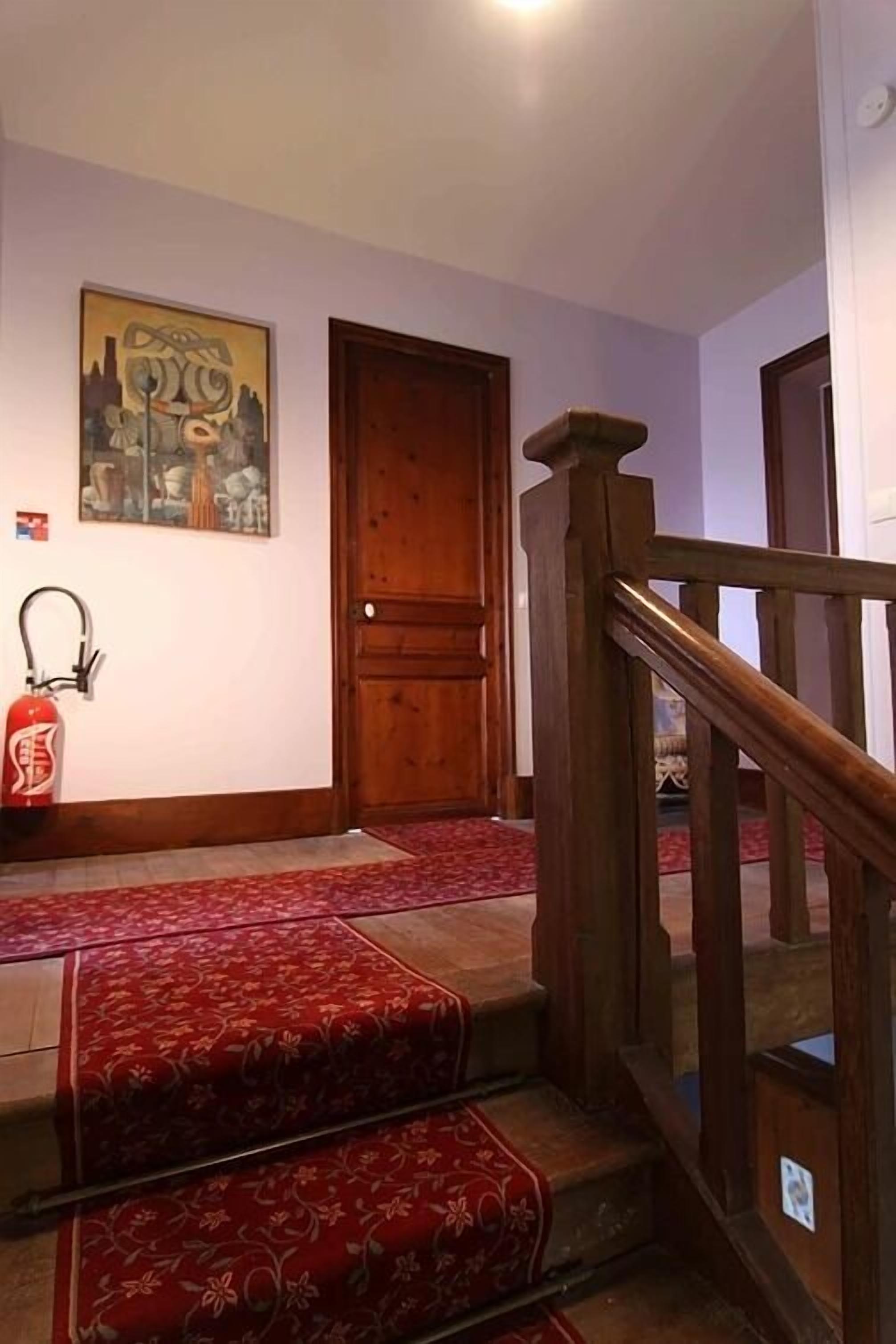 A staircase with a wooden handrail and red carpeted steps leading to a wooden door.