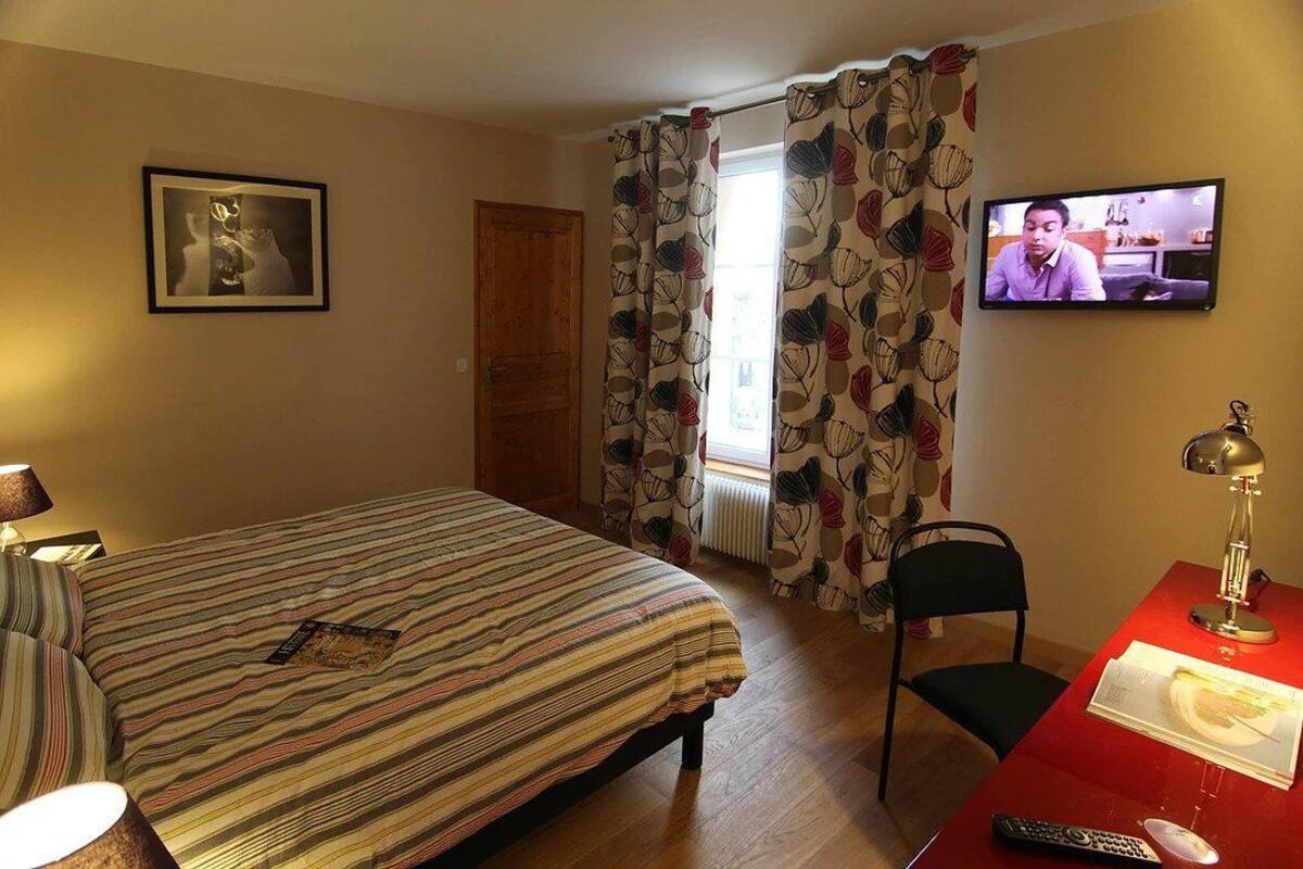 A hotel room with a bed, a desk with a lamp, a chair, a television, and a window with curtains.