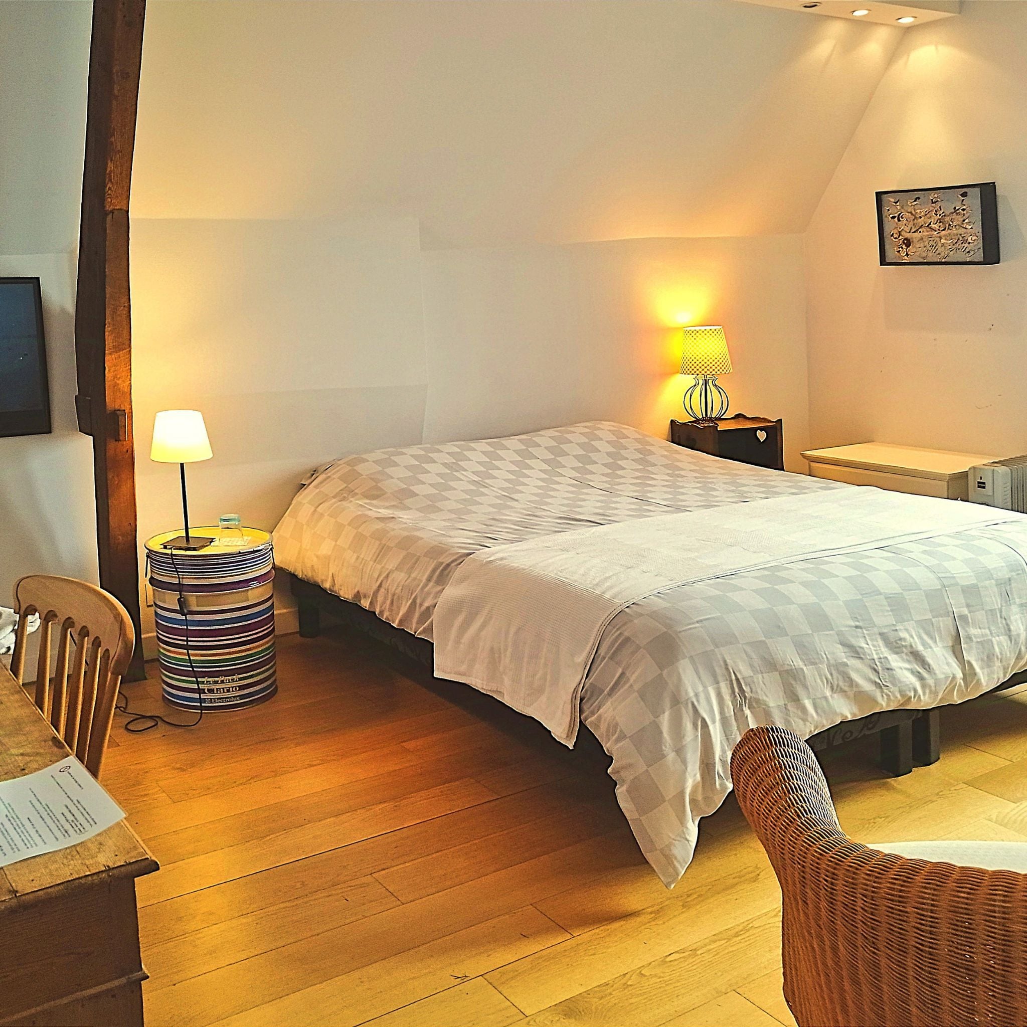 Un dormitorio con cama, mesita de noche, lámpara, silla y una pequeña mesa con un recipiente a rayas.