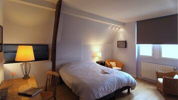 Een hotelkamer met een groot bed, een stoel, een tafel met een lamp en een raam.