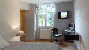 A bedroom with a bed, a desk, a chair, a TV, and a window with curtains. - Les Tourelles de Thun (Meulan-en-Yvelines)