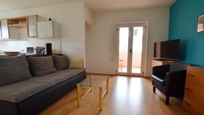 Ett modernt vardagsrum med en soffa, ett soffbord, en TV och en skjutdörr i glas som leder ut till ett utomhusområde.