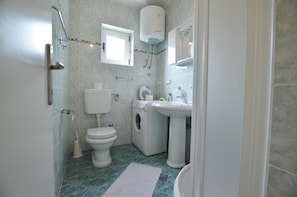 A compact bathroom with a toilet, washing machine, sink, and a small window. - Kliska Apartment (Rovinj)