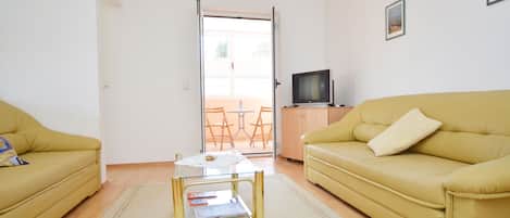 A living room with a yellow sofa, a glass coffee table, and a television on a stand.