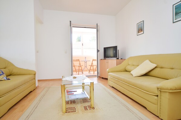 A living room with a yellow sofa, a glass coffee table, and a television on a stand. - Kliska Apartment (Rovinj)