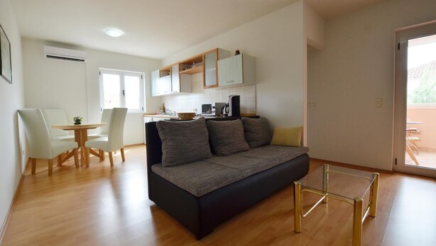 Ett modernt vardagsrum med en soffa, ett matbord med stolar, en köksdel och en skjutdörr i glas som leder ut till uteplatsen.