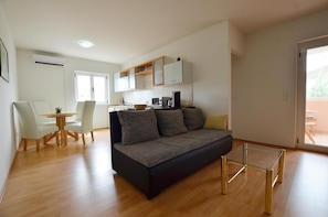 Een moderne woonkamer met een bank, een eettafel met stoelen, een keukenhoek en een glazen schuifdeur naar buiten.