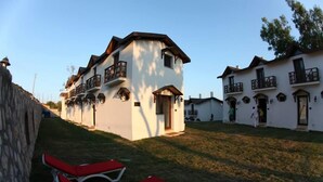 A row of white buildings with balconies, a stone wall, and red lounge chairs. - Karaburun Mimoza Apart Hotel (Karaburun)