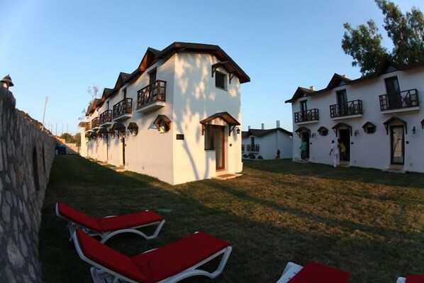 Filas de edificios blancos con balcones, un muro de piedra y sillones rojos.