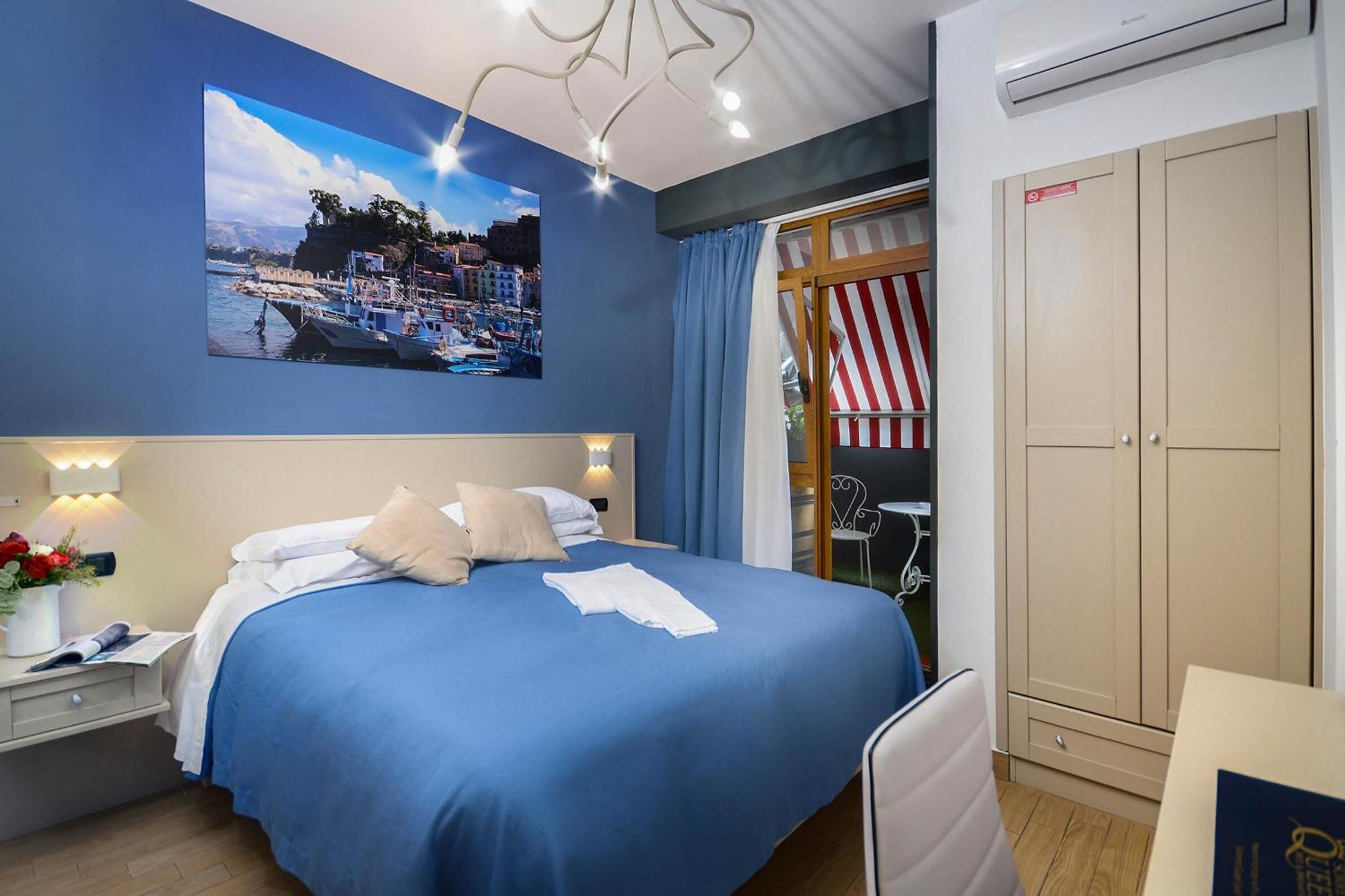 Une chambre bien rangée, avec un lit, une table de chevet, une lampe et une grande fenêtre avec des rideaux.