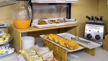 Ein Frühstücksbuffet mit verschiedenen Backwaren, einer Kaffeemaschine und einem Saftspender.