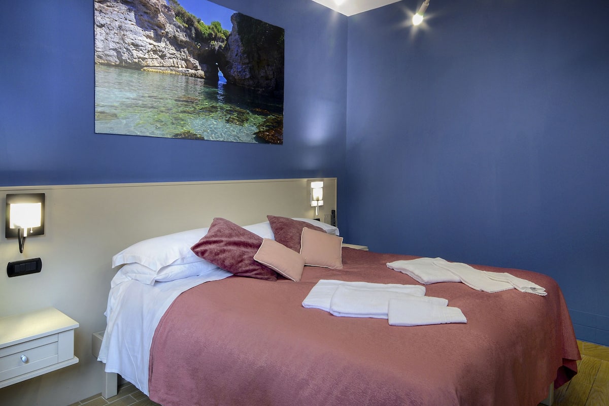 Une chambre à coucher avec un lit, des oreillers, une table de chevet et une lampe fixée au mur.