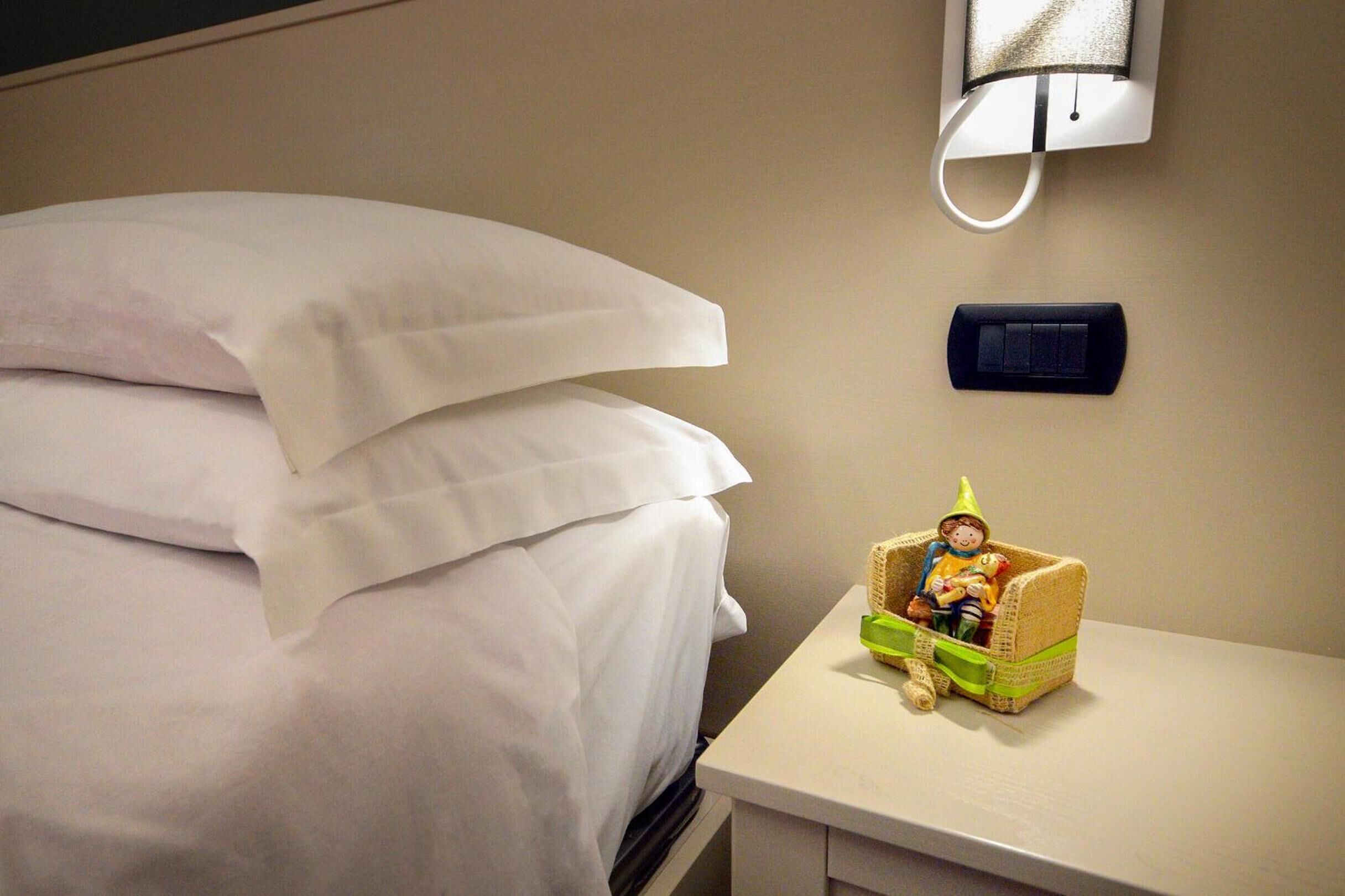 Un letto rifatto con lenzuola bianche, un comodino con una statuina e un lampadario a parete.