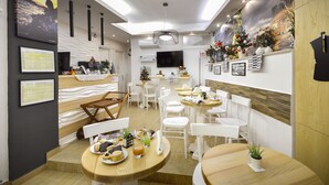 Un hall d’hôtel moderne avec des tables rondes, des chaises blanches, un téléviseur à écran plat et une fresque murale.