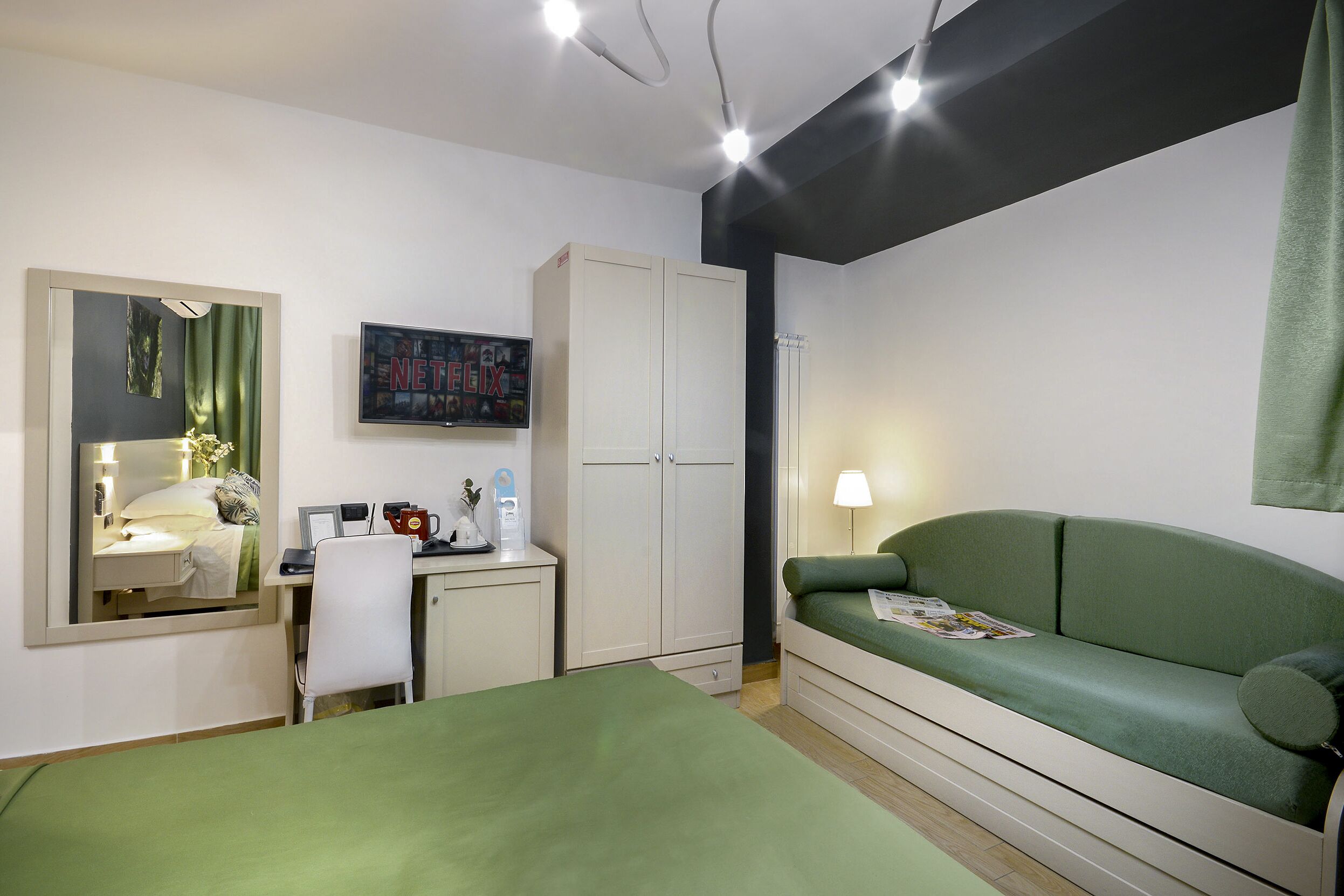 Ein Schlafzimmer mit einem Bett, einem Schreibtisch, einem Stuhl, einem Kleiderschrank und einem grünen Sofa.