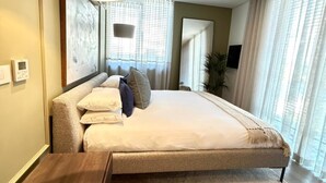 A modern bedroom with a large bed, a bedside table, a hanging light fixture, and a view through the window. - Warwick 501 (Cape Town)