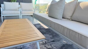 A modern outdoor seating area with a wooden table, white cushioned chairs, and a sofa with multiple pillows. - Warwick 501 (Cape Town)