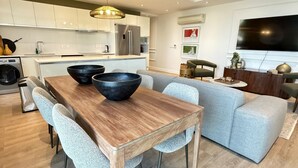 A modern kitchen with white cabinets, a dining table with chairs, and a grey sofa in the living area. - Warwick 501 (Cape Town)