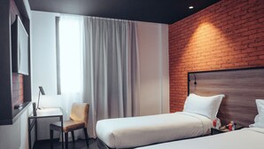 Een hotelkamer met twee bedden, een bureau, een stoel en een groot raam met gordijnen.