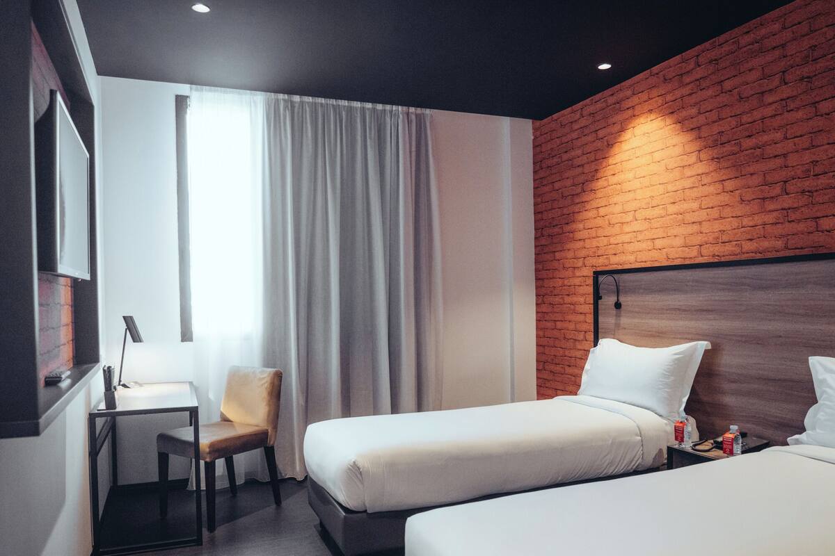 Ein Hotelzimmer mit zwei Betten, einem Schreibtisch, einem Sessel und einem großen Fenster mit Vorhängen.