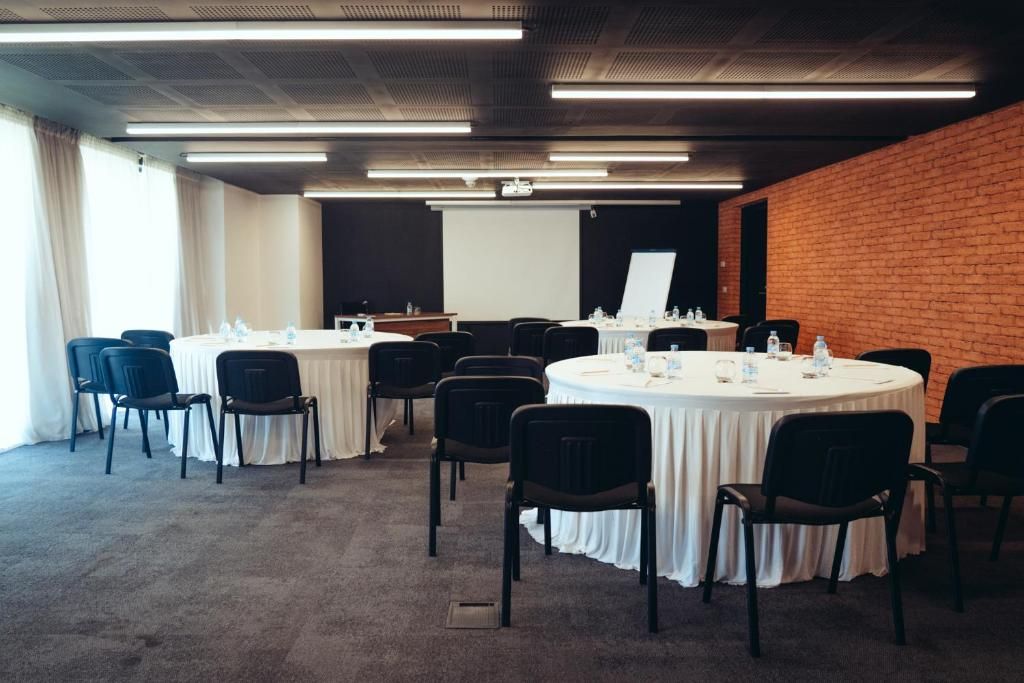 Une salle de conférence équipée de tables rondes, de chaises et d’un écran de projection.